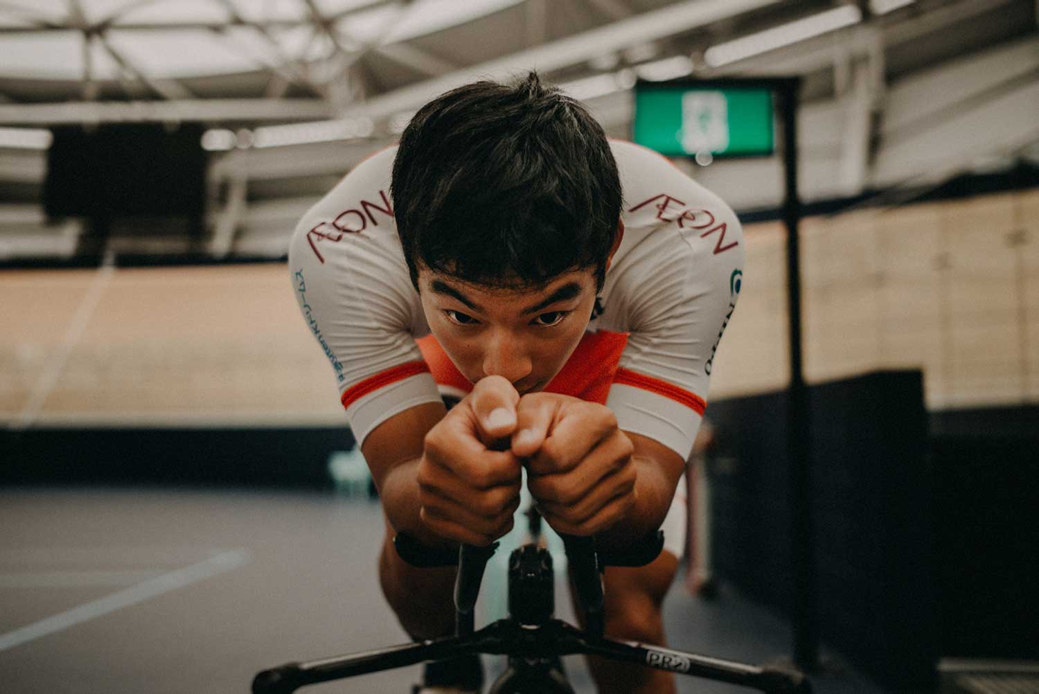 Japanese cyclist trains on aerobars of staic bike in velodrome during training session