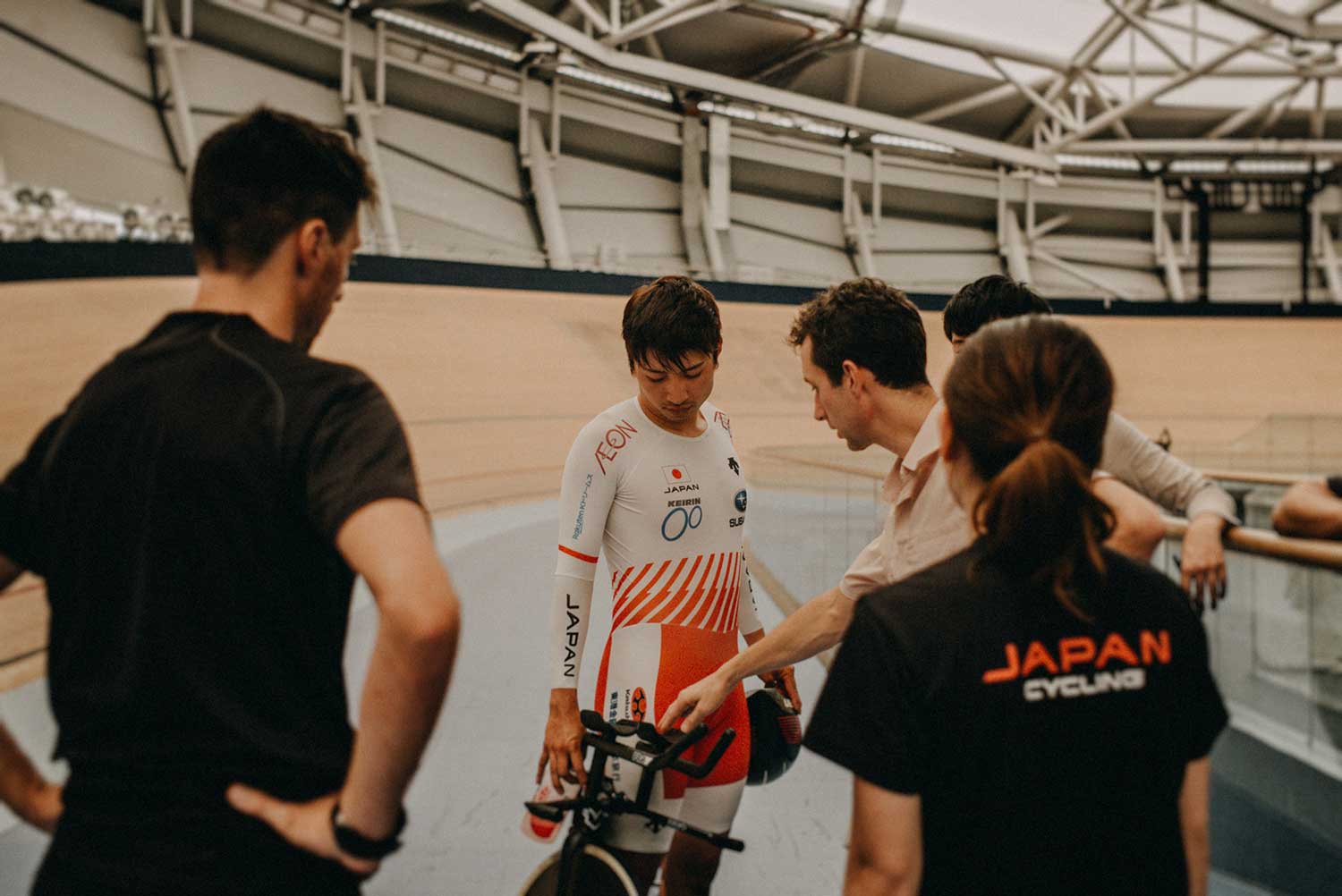 Japanese cyclist discusses performance with coaches after training in velodrome